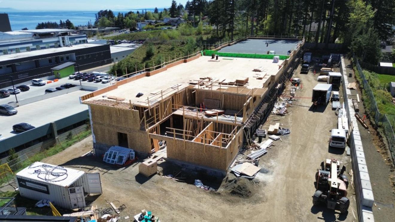 Construction site with a partially built wooden structure surrounded by vehicles and trees.