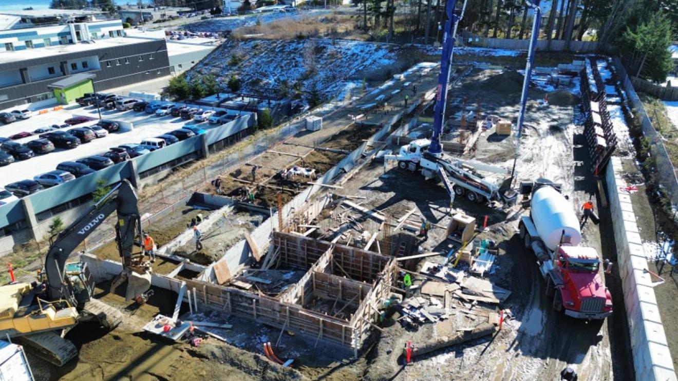 Construction site with workers, machinery, and foundations being laid in a mixed-use area.