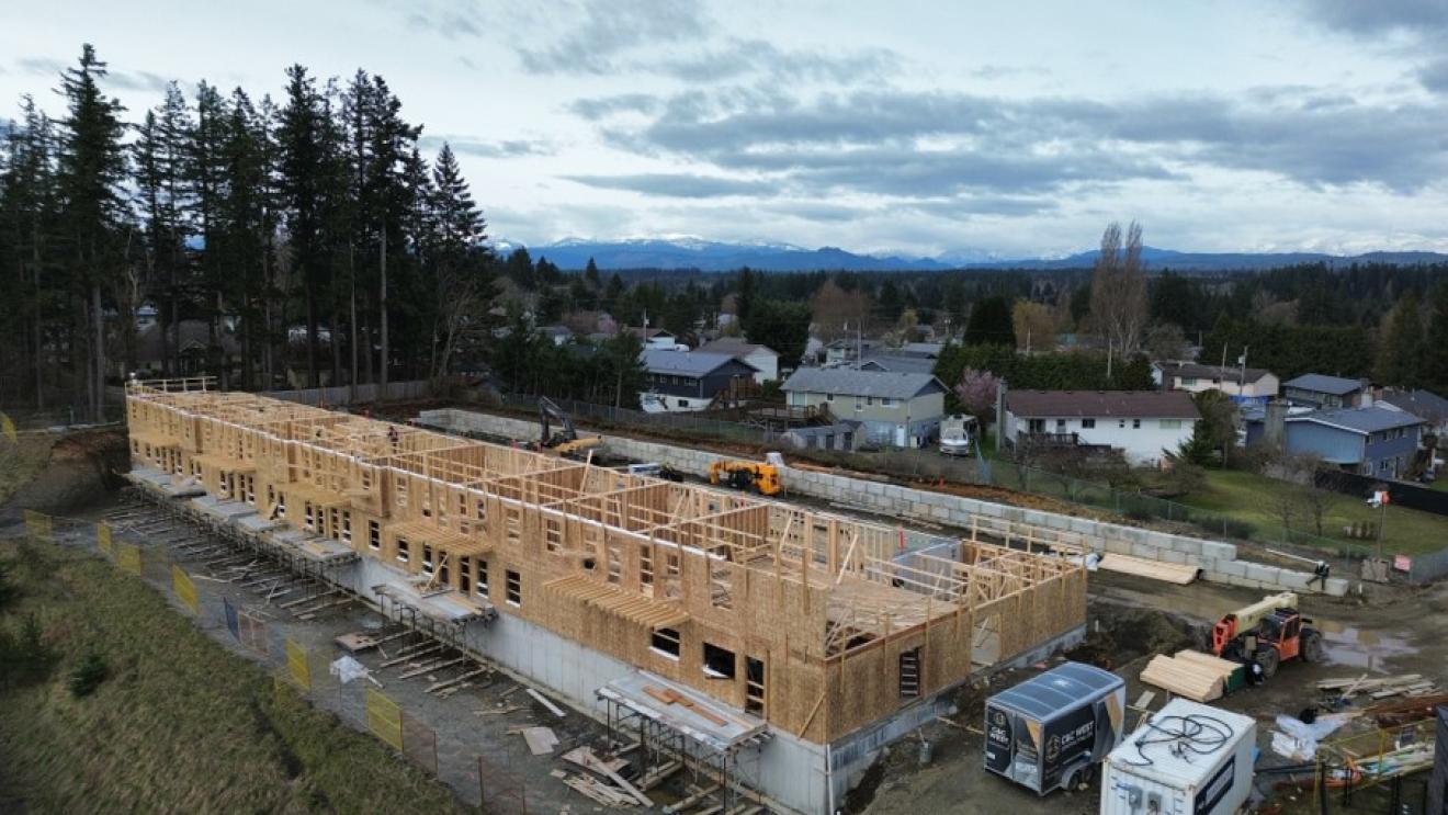 Construction site of a multi-unit building with wooden frames and surrounding houses.