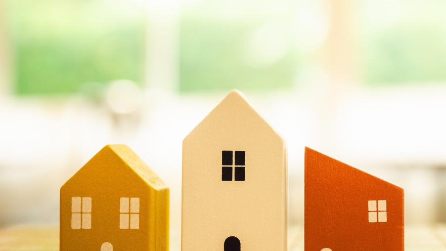 Small wooden house models in yellow, white, and orange on a wooden table.