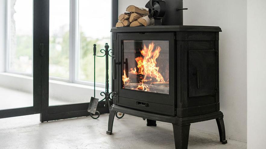 Cozy wood stove with fire burning, logs stacked on top, near large windows.