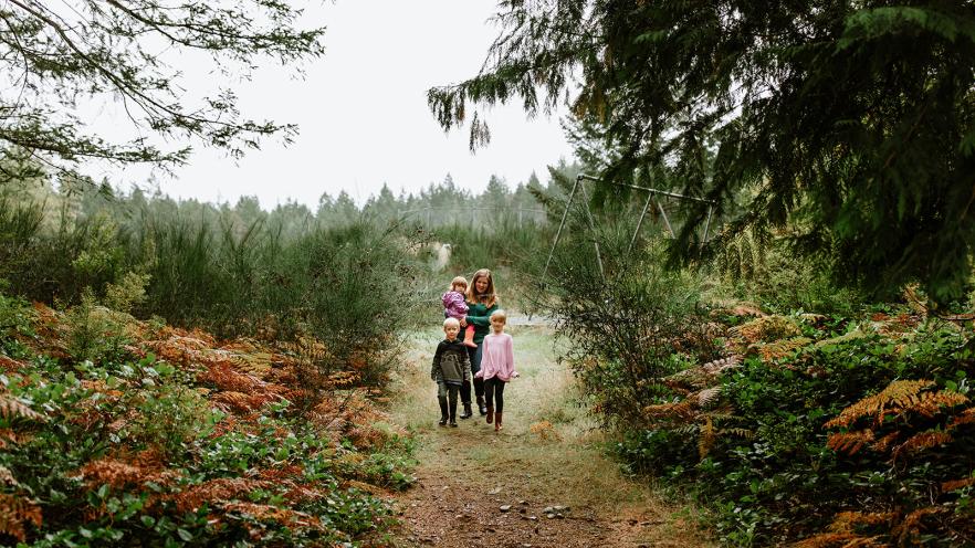 A woman and two children walk along a forest path, surrounded by greenery and autumn foliage.