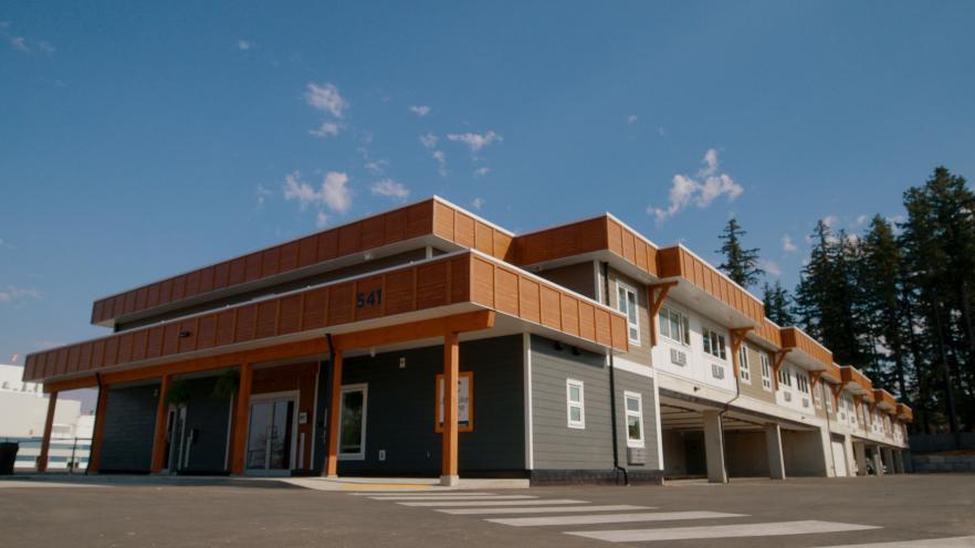 Modern building with wooden accents and large windows, set against a blue sky.