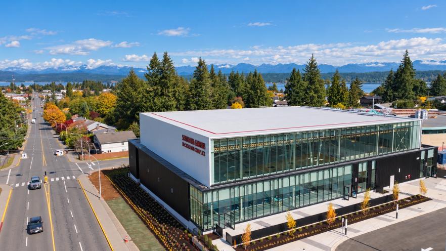 Modern building with large windows, surrounded by trees and mountains in the background.