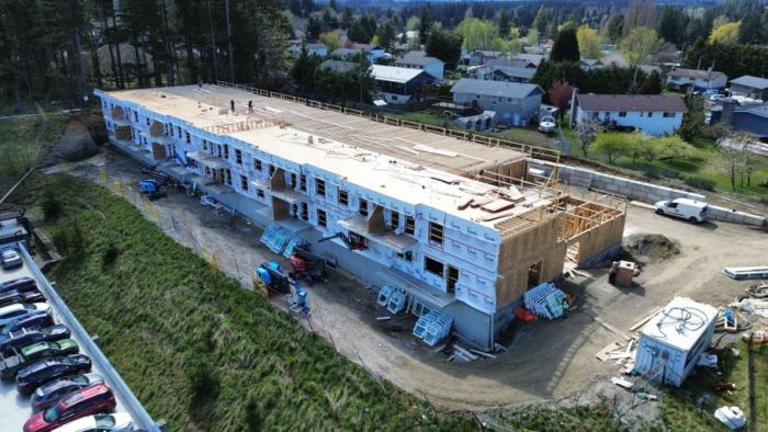 Aerial view of a building under construction, surrounded by parked cars and houses.