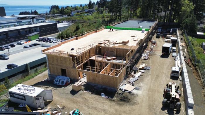 Construction site with a partially built wooden structure surrounded by vehicles and trees.