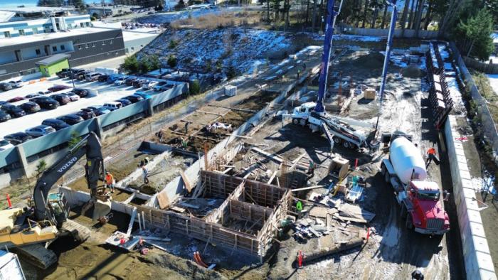 Construction site with workers, machinery, and foundations being laid in a mixed-use area.