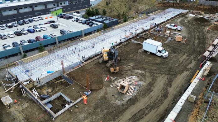 Construction site with machinery, foundations, and parked vehicles in a busy area.