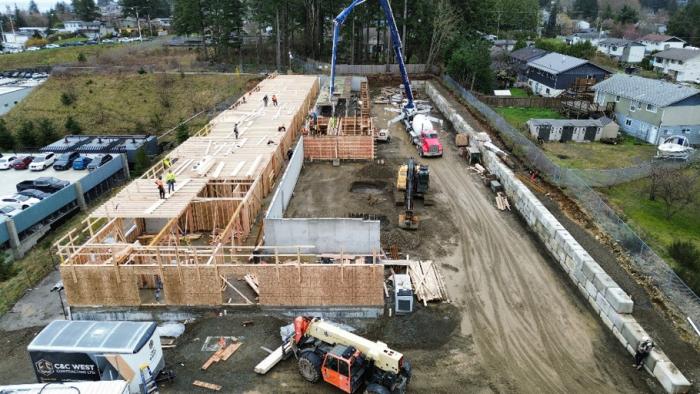 Construction site with wooden frames, machinery, and nearby buildings.