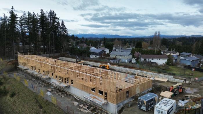 Construction site of a multi-unit building with wooden frames and surrounding houses.