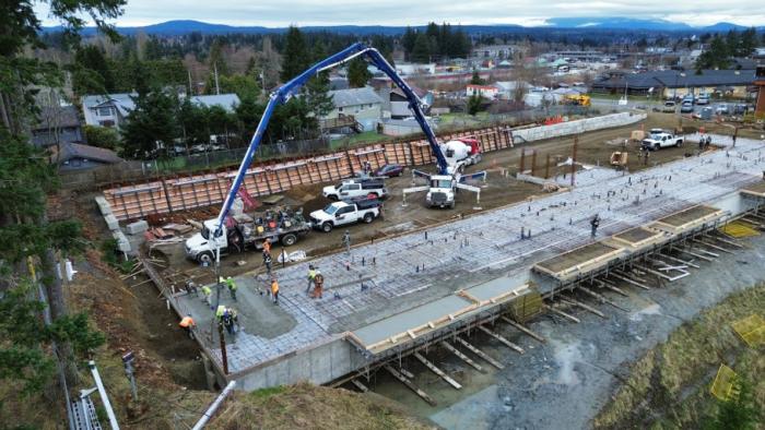 Construction site with machinery, foundations, and parked vehicles in a busy area.