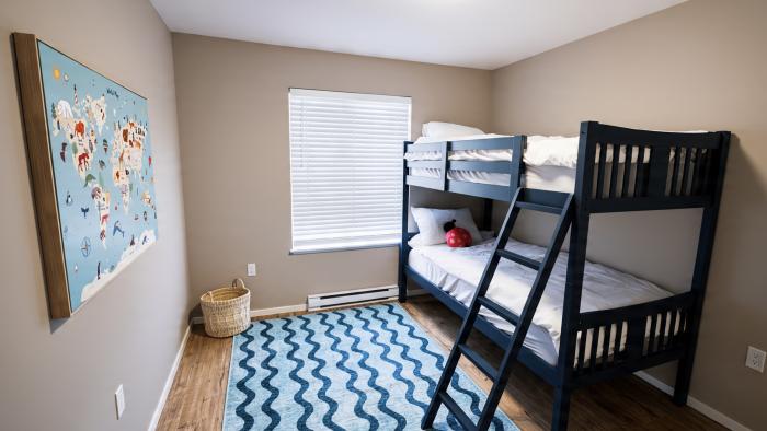 Child's bedroom with a blue bunk bed, striped rug, and a colorful world map on the wall.