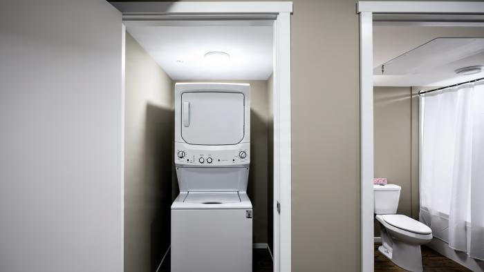 Laundry machines stacked in a small room with a bathroom visible in the background.