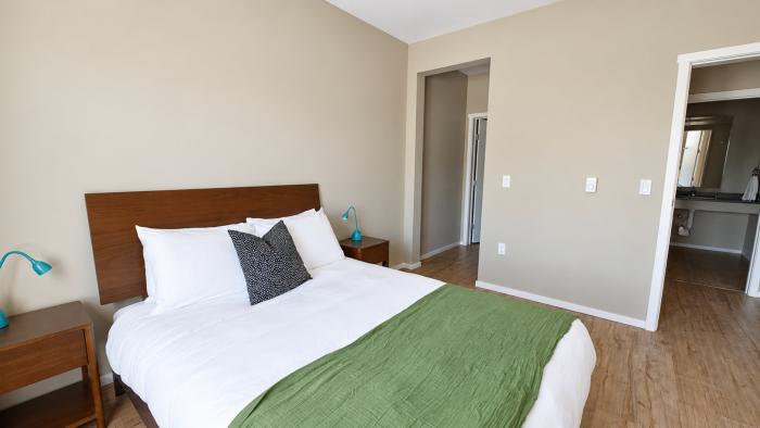 Bright bedroom with a double bed, green throw, and wooden furniture.