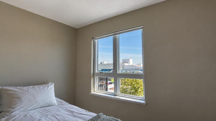 Bright bedroom with a bed, soft linens, and a window showing a clear sky and trees outside.