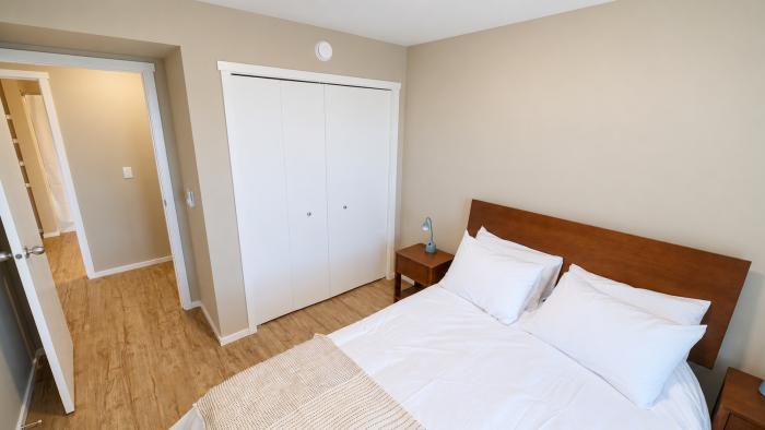 Cozy bedroom with a wooden bed, white bedding, and closet, light beige walls, and wooden floor.