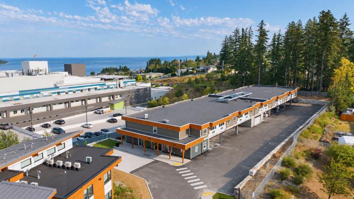 Aerial view of a modern building with orange accents, surrounded by trees and a glimpse of water.