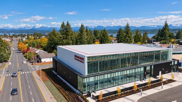 Modern building with large windows, surrounded by trees and mountains in the background.
