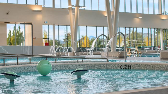 Indoor swimming pool with water features, large windows, and green floating toys.