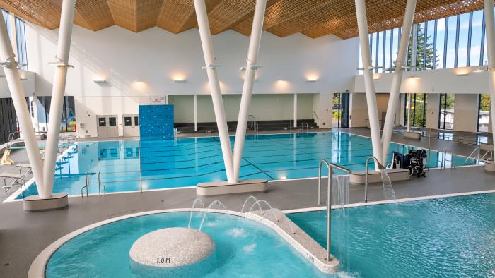 Indoor swimming pool with large windows, a hot tub, and modern architectural features.
