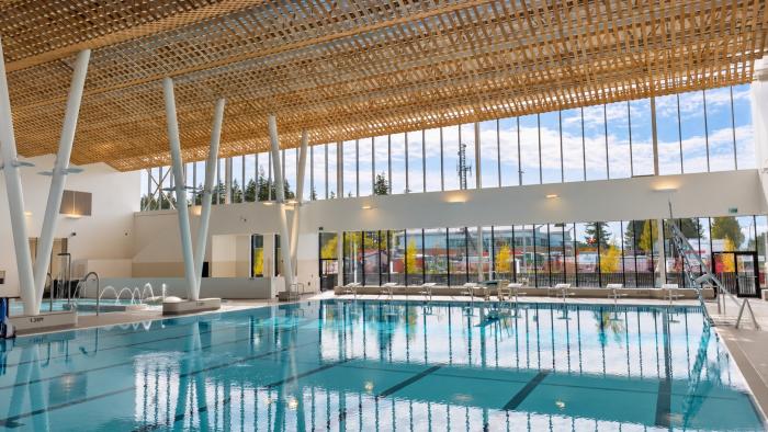 Bright indoor swimming pool with large windows and wooden ceiling beams.