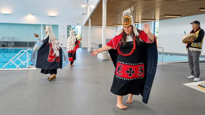 A group of dancers in traditional attire perform inside a spacious, brightly lit venue.