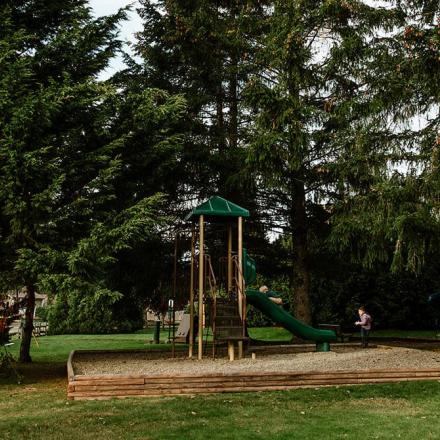 Playground surrounded by tall trees, with a slide and a wooden structure.