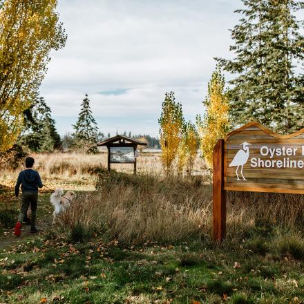 Trail entrance with wooden park sign amidst autumn trees.