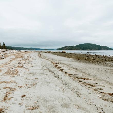 Sandy beach with distant hills under a cloudy sky.