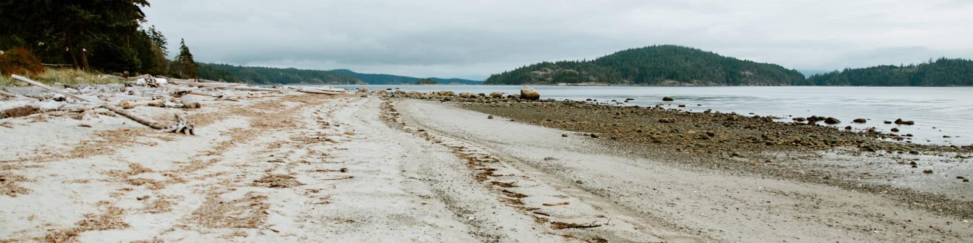 Sandy beach with distant hills under a cloudy sky.