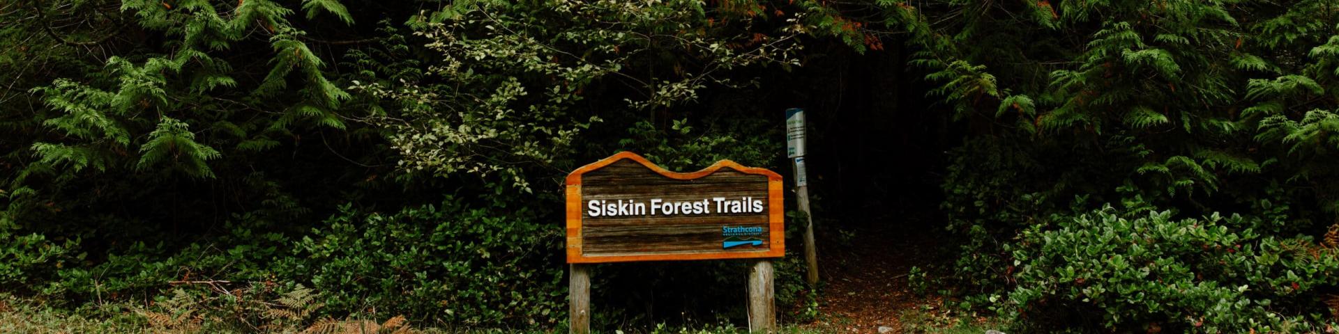 Trailhead sign surrounded by dense green foliage.