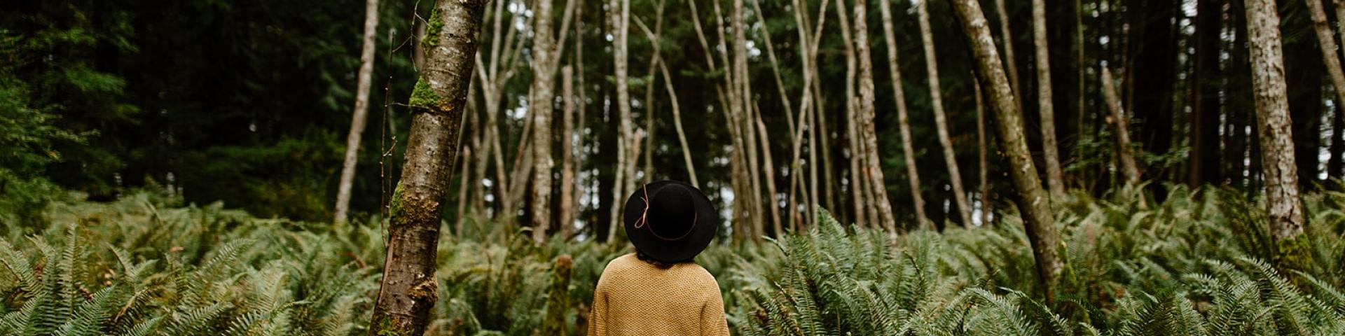 Person in a yellow coat walking through a dense forest path.