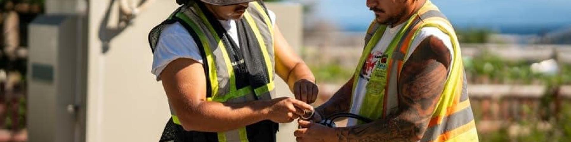 Two workers in reflective vests handling cables outdoors.