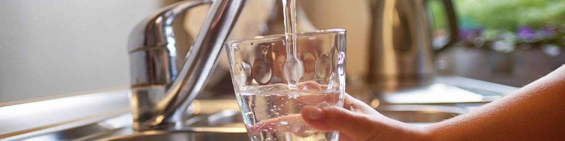 Hand holding glass filling with water from kitchen faucet.