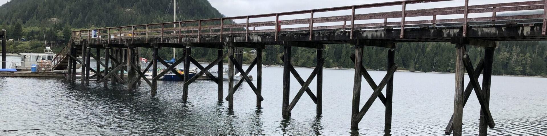 Wooden pier extending over calm water, with a mountainous backdrop and cloudy sky.