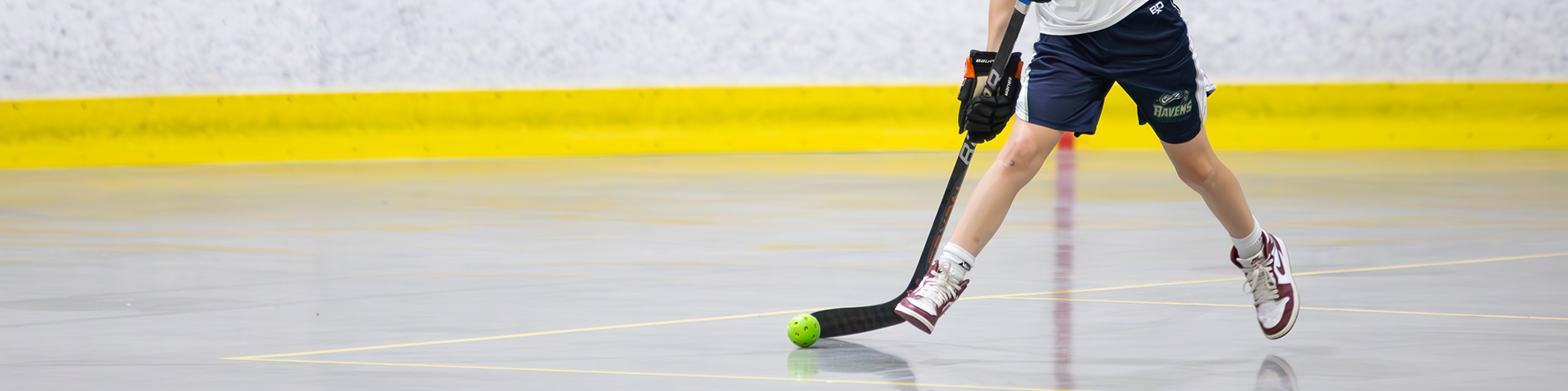 View of feet and hockey stick of a child playing floor hockey on the arena dryfloor