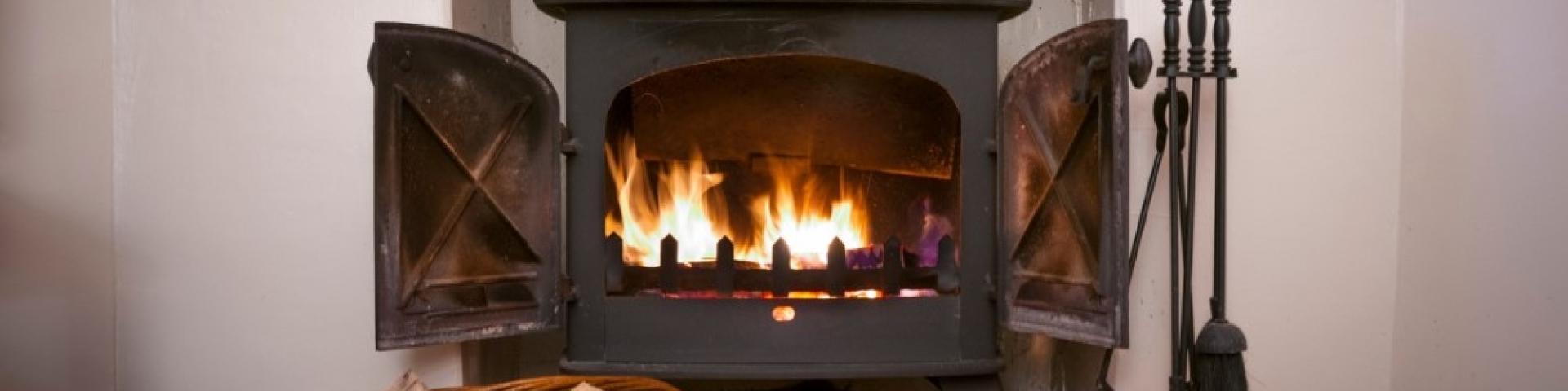 Cozy fireplace with open doors, wood logs, and flames inside.
