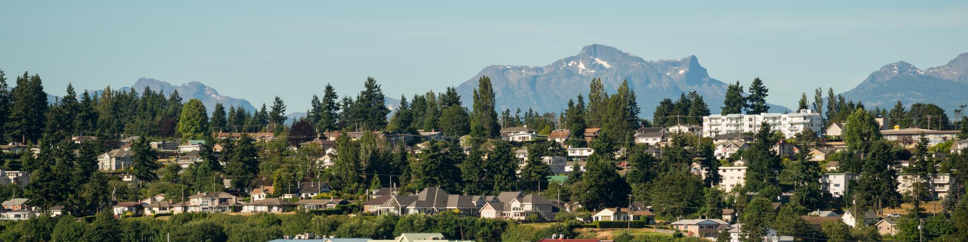 Coastal town with green hills and mountains in the background under a clear blue sky.