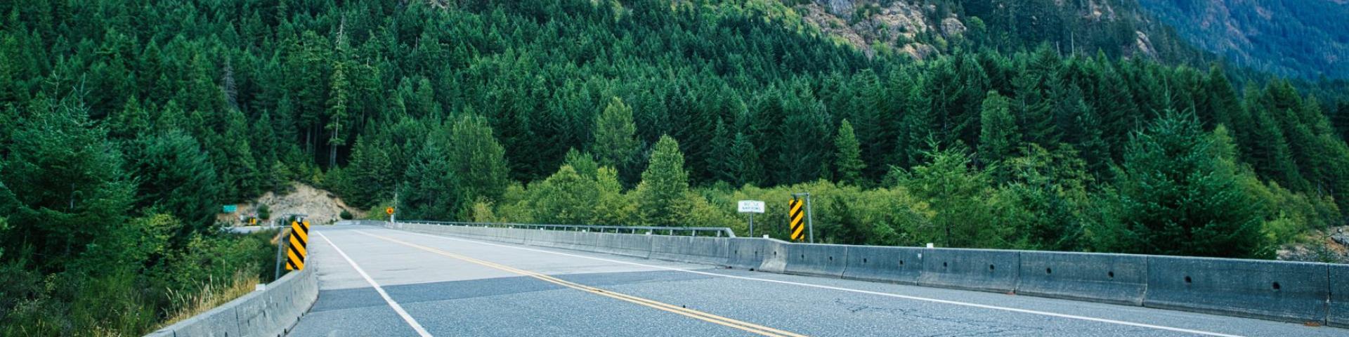 Scenic road winding through lush greenery with mountains and a colorful sunset.