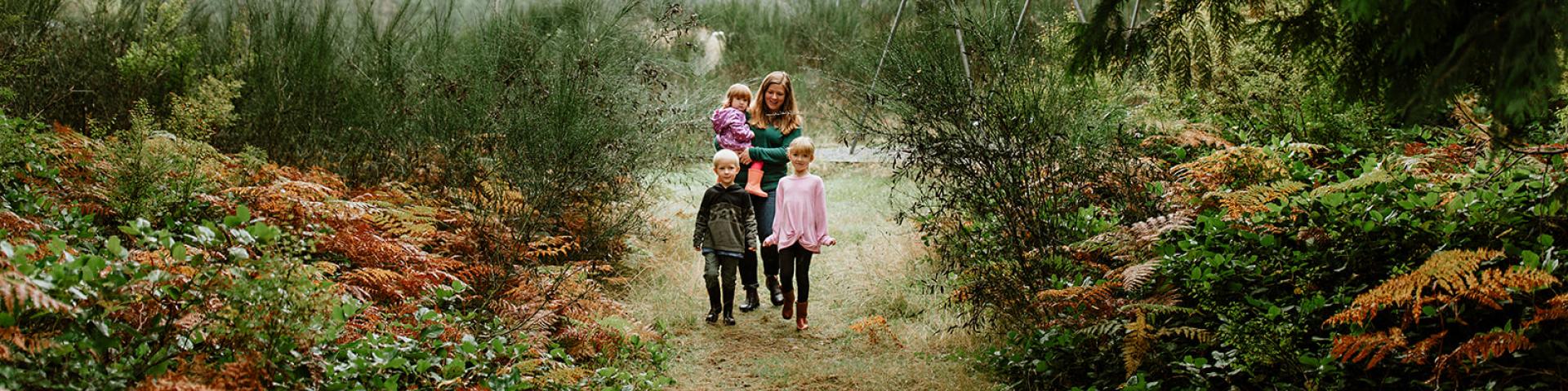 A woman and two children walk along a forest path, surrounded by greenery and autumn foliage.