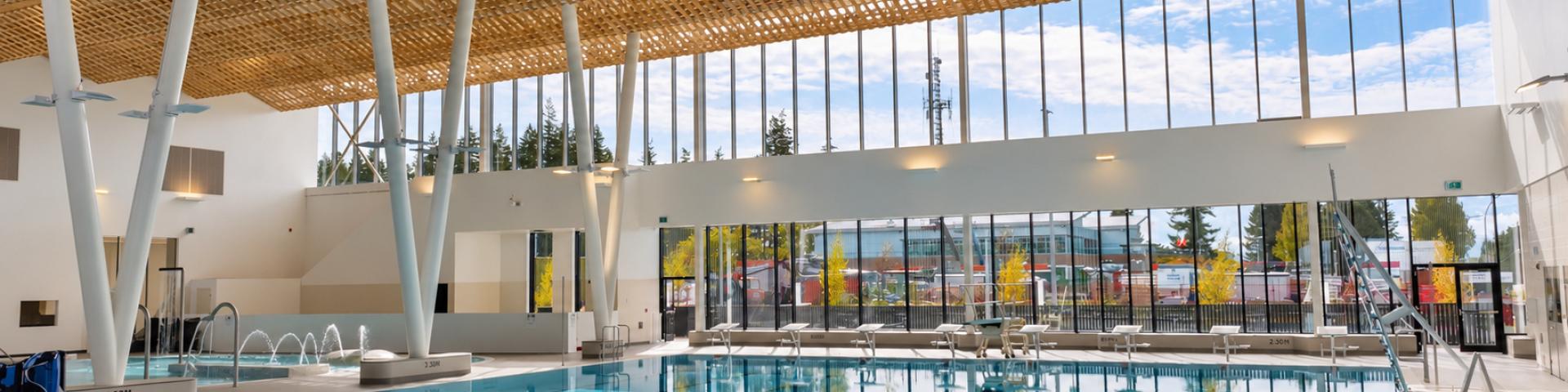 Bright indoor swimming pool with large windows and wooden ceiling beams.