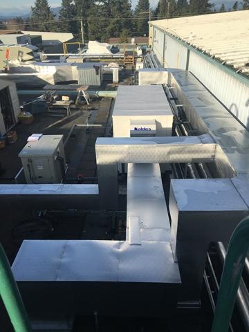 Silver ductwork on a rooftop with trees in the background.