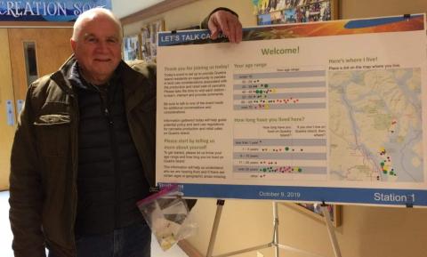 Electoral Area C Director, Jim Abram next to an informational display board indoors.