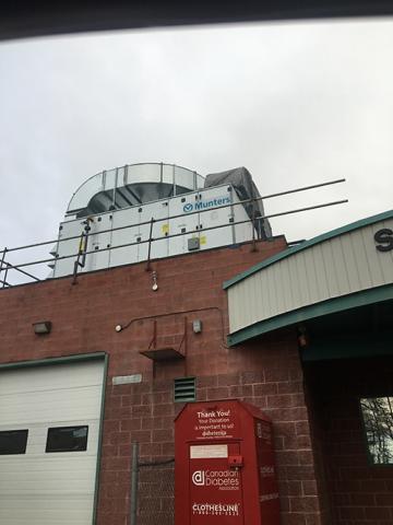 Brick building with rooftop equipment and a red donation bin nearby.