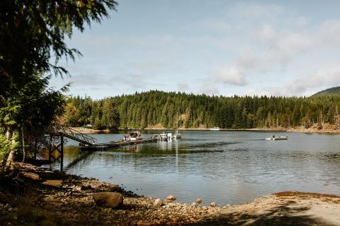 Lake with wooden dock, surrounded by forest under a partly cloudy sky.