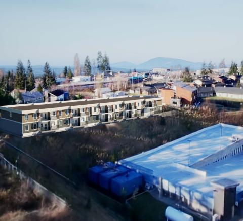 Aerial view of a modern building complex surrounded by trees and distant mountains.