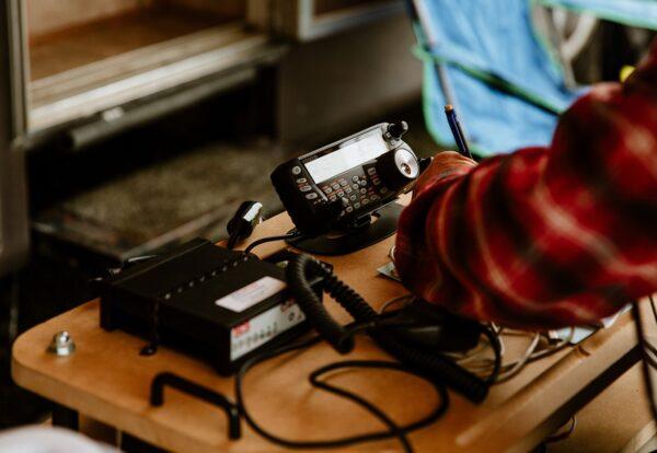 Radio equipment on a wooden table being adjusted by a person in a plaid shirt.