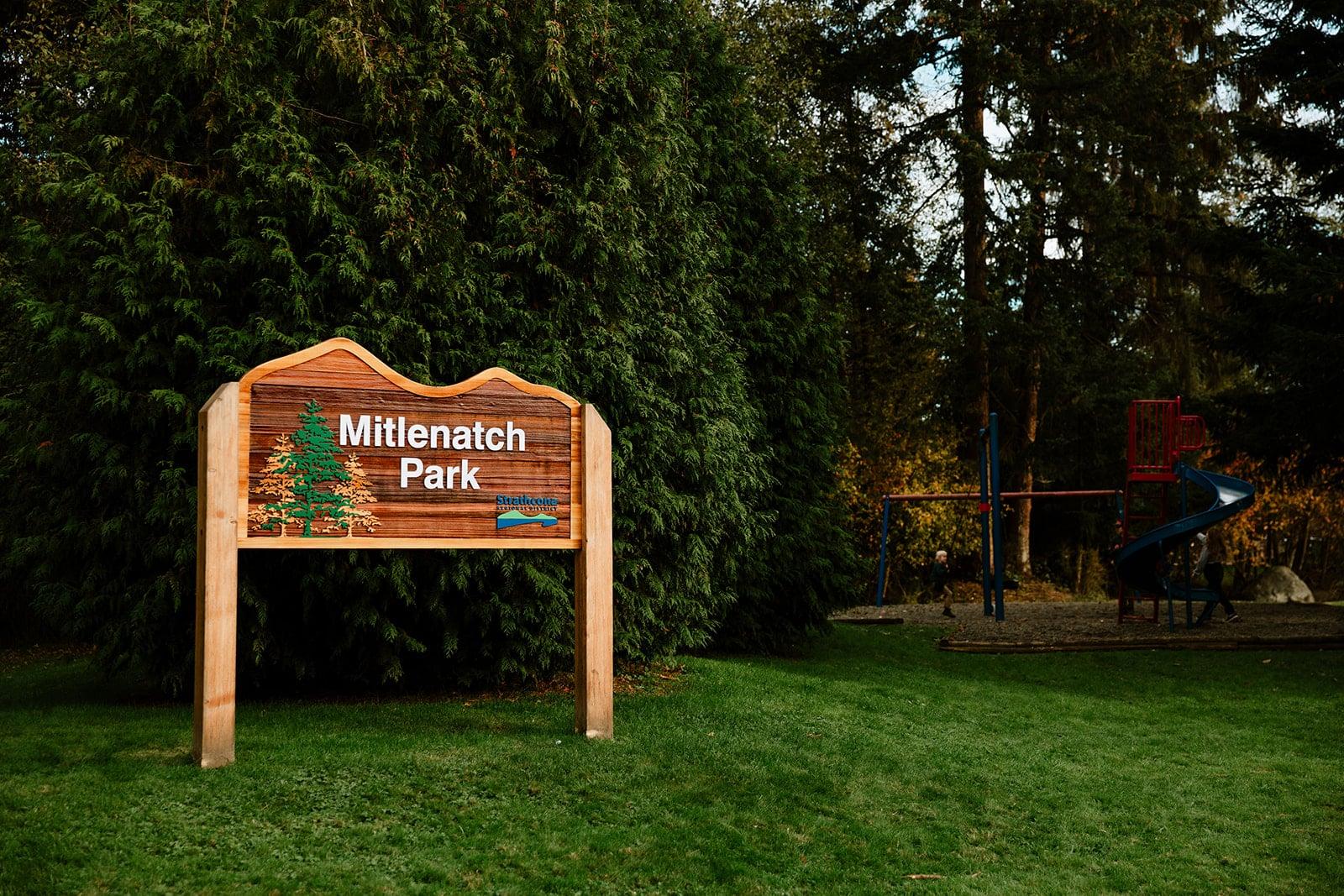 Sign reading "Miner's Park" with trees and playground in the background.