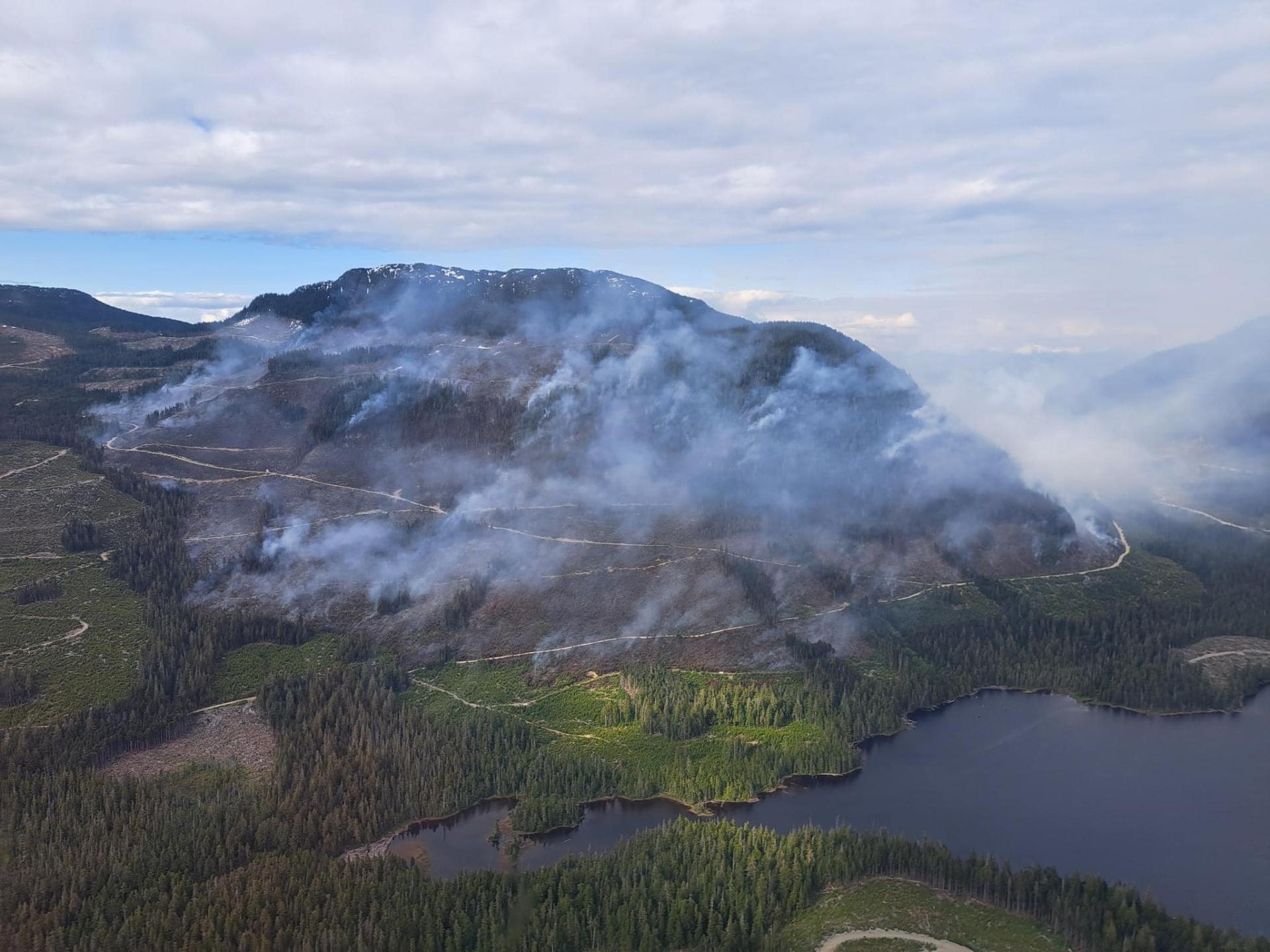 Smoke rising from a mountain wildfire, with a lake in the foreground.