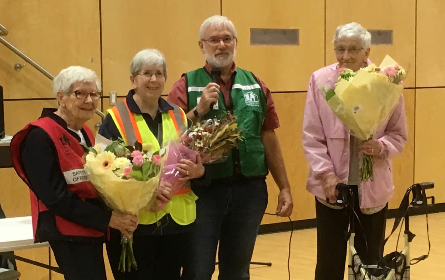 Four seniors with bouquets smiling in a gymnasium setting.